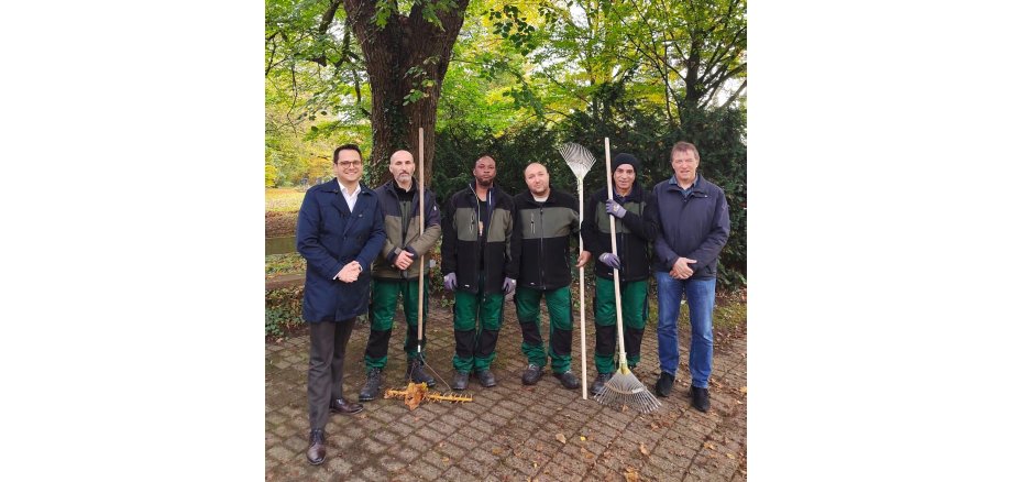 Gruppenbild der Geflüchteten im Einsatz mit Dr. Benjamin Fadavian (li.) und Rainer Schulte, Abteilungsleiter des Bereichs Grünflächen/Friedhöfe/Baubetrieb